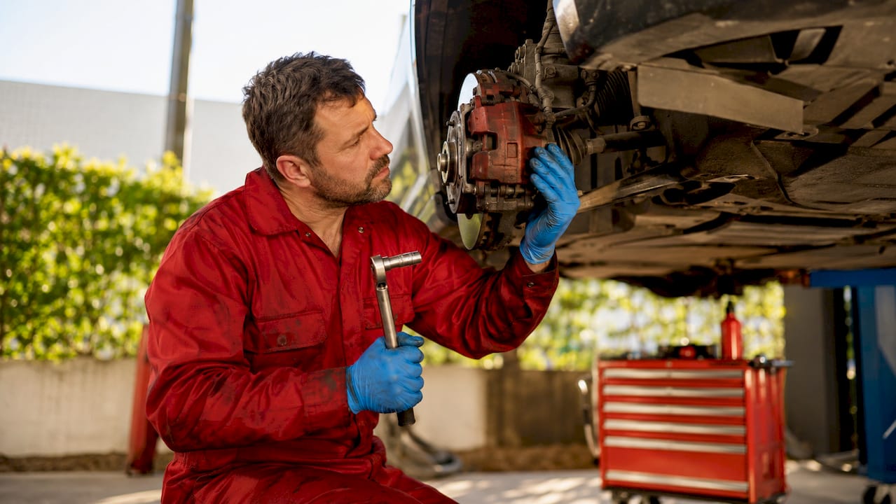 Technician inspecting brake caliper on vehicle wheel