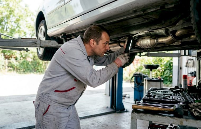 Mechanic inspecting car exhaust system under vehicle