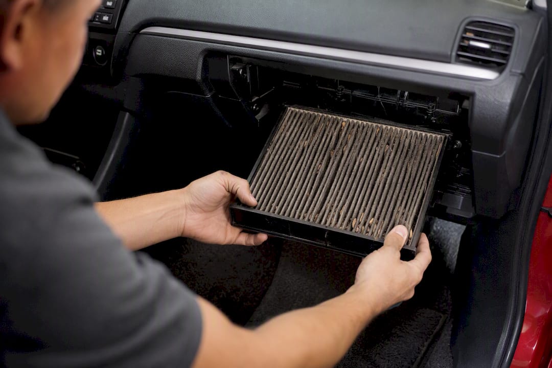 Hands removing dusty cabin air filter