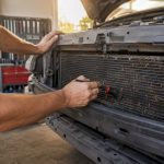 Hands clearing debris from car condenser fins
