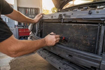 Hands clearing debris from car condenser fins