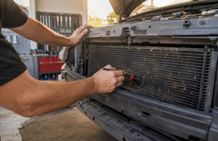 Hands clearing debris from car condenser fins